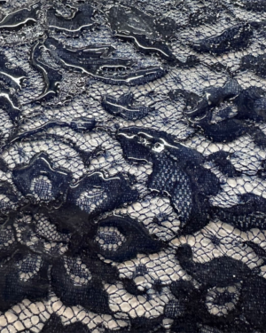 Gros plan sur une innovation textile : dentelle siliconée bleu sur résille fine, montrant la texture brillante et translucide du silicone injecté, effet sculpté en relief.